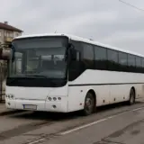 Un autobuz alb, modern, oprit într-o stație de transport public dintr-o zonă care pare rurală sau periferică