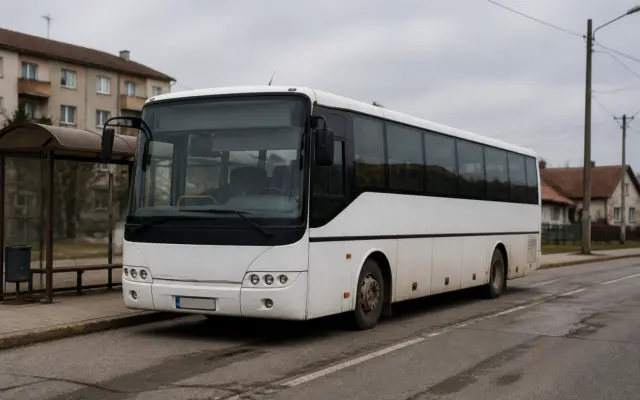 Un autobuz alb, modern, oprit într-o stație de transport public dintr-o zonă care pare rurală sau periferică