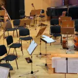Empty chairs, music stands, and orchestral instruments arranged on a stage for a symphonic concert