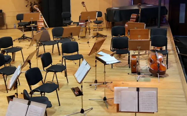 Empty chairs, music stands, and orchestral instruments arranged on a stage for a symphonic concert