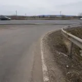 O imagine care surprinde un drum local asfaltat ce se curbează spre dreapta pentru a se intersecta cu o șosea de centură (drum cu mai multe benzi)