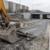 Un braț și o cupă de excavator în prim-planul unui șantier rutier, unde se văd bucăți de asfalt proaspăt excavat