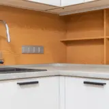Un robinet de bucătărie modern, cromat, situat lângă o chiuvetă neagră într-o bucătărie cu blat gri și fundal din panouri de lemn