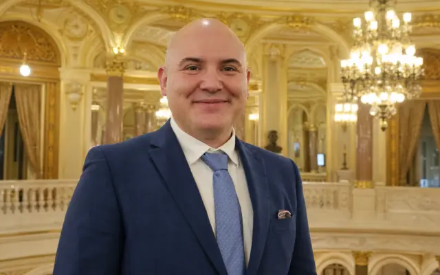 Portrait of a smiling bald man in a suit standing in front of a Gala Premiilor MUSICRIT backdrop