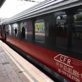 Un vagon de tren CFR Călători, de culoare roșu cu negru, oprit la peronul unei gări