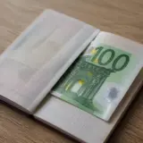 Un pașaport deschis pe o masă de lemn, în interiorul căruia se află o bancnotă de 100 de euro de culoare verde
